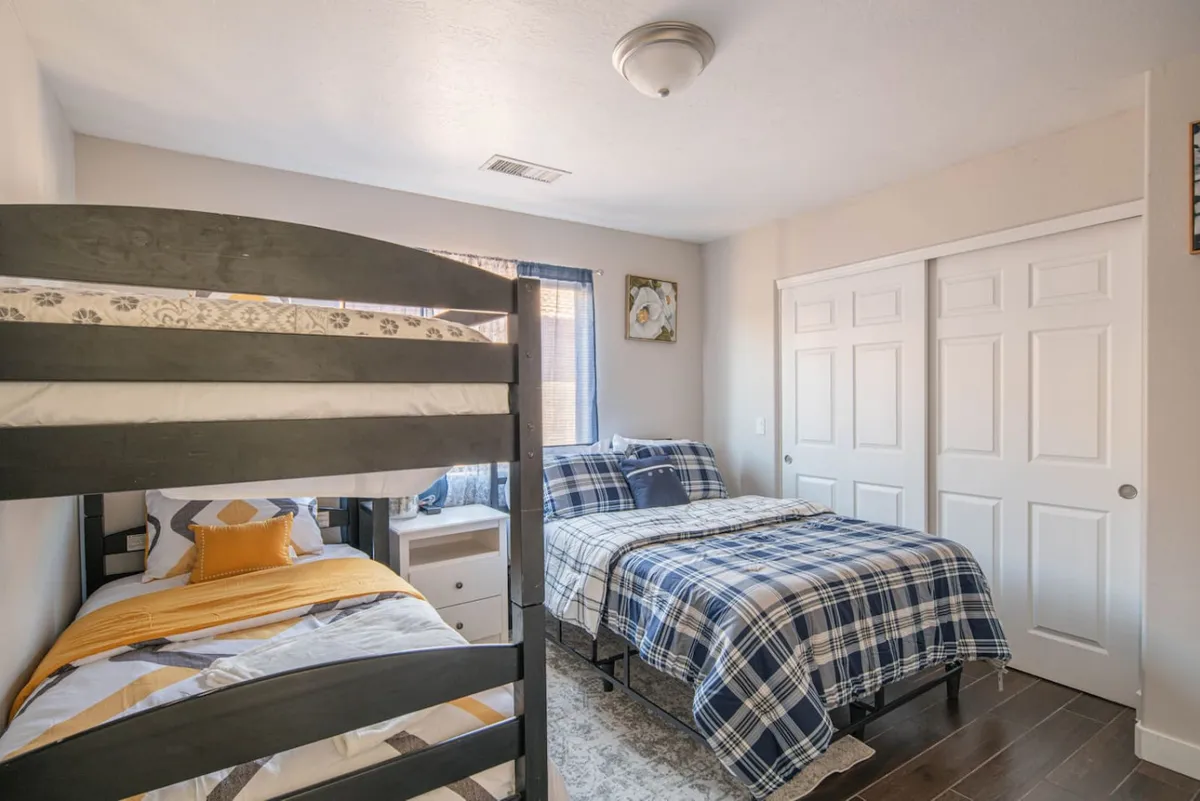 A cozy, family-friendly bedroom featuring a double bed and a bunk bed, both with plaid bedding. A nightstand with a lamp adds to the relaxed ambiance, and the setup caters perfectly to kids or group travelers.