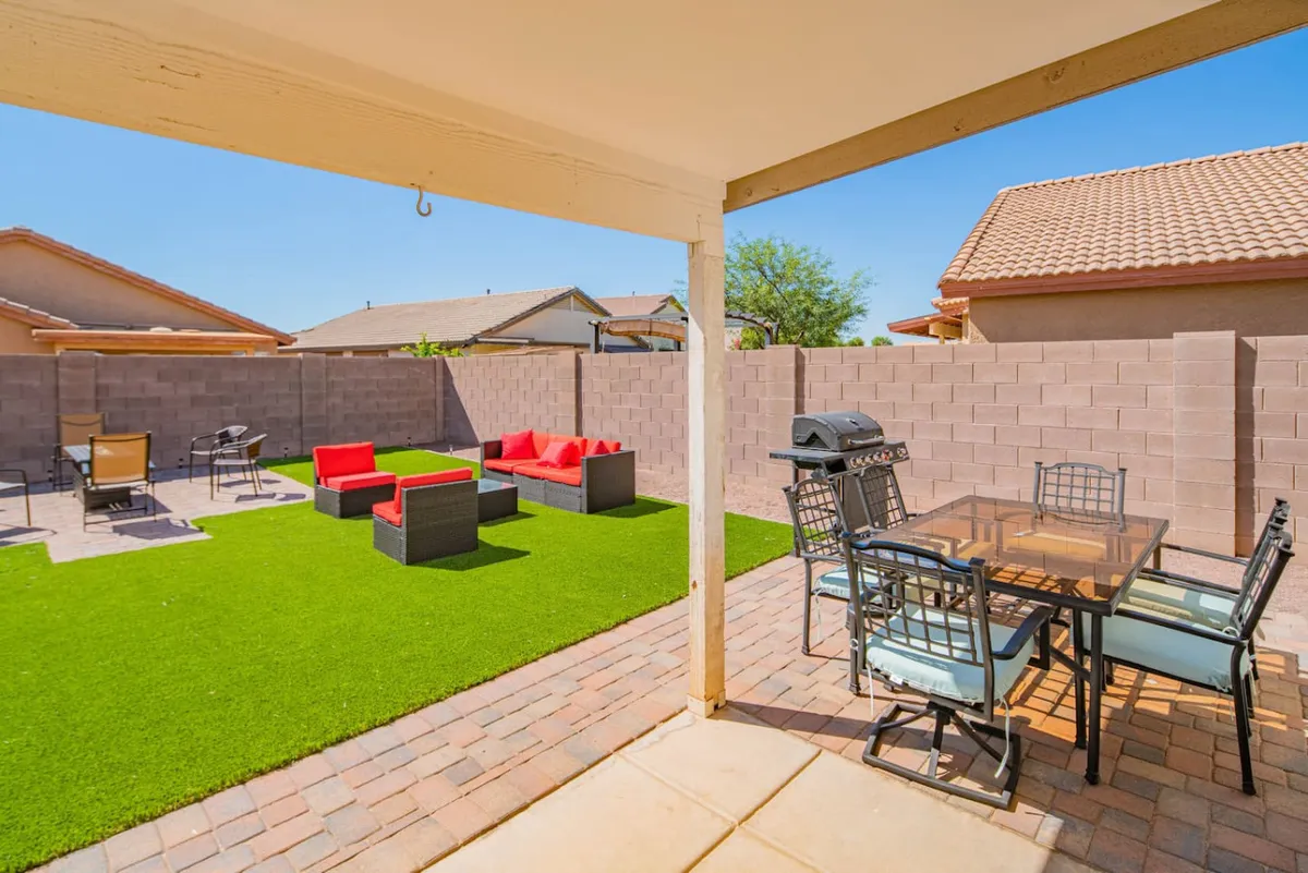 A welcoming backyard setup with a BBQ grill, dining table with vibrant red seating, a lush green lawn, and a generous patio area. The space is arranged for outdoor dining and grilling, perfect for both family meals and lively social events.