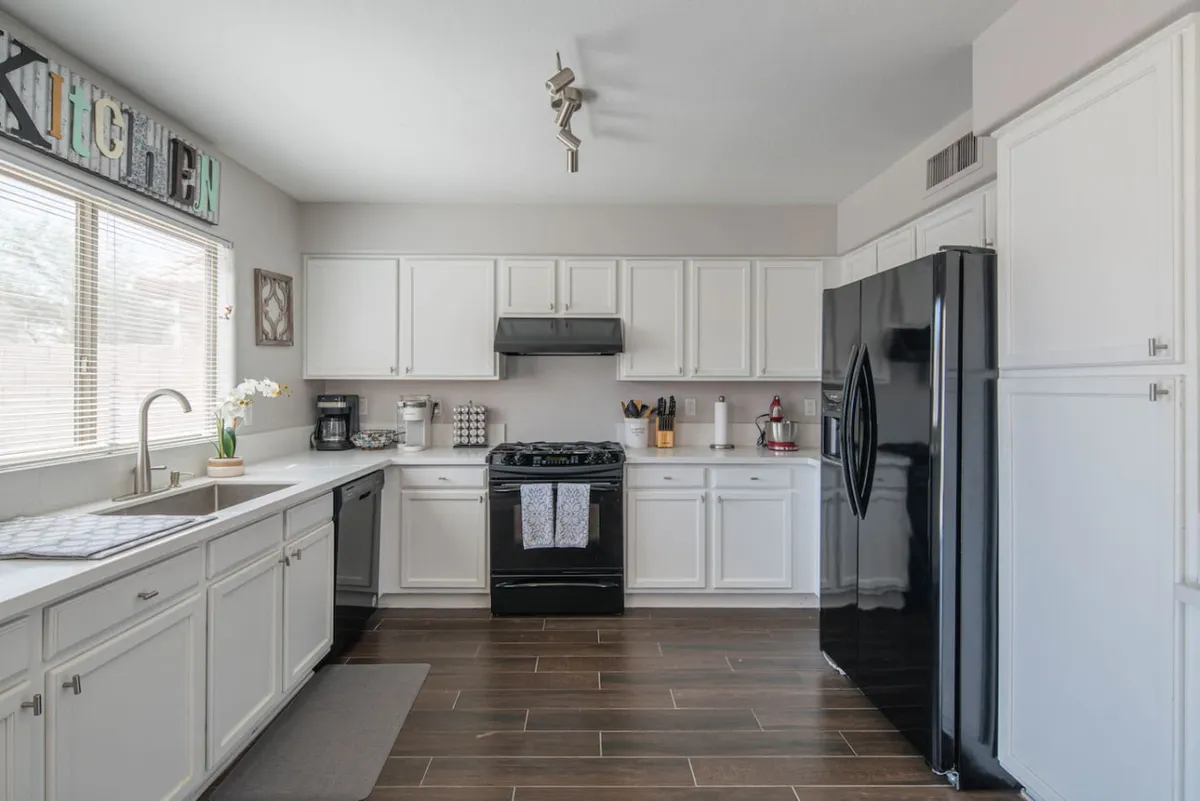 A bright, spacious kitchen featuring crisp white cabinetry, sleek black appliances, ample counter space, and a window that lets in natural light. The setup includes a modern stove, refrigerator, and space for meal prep, perfectly matching the atmosphere of a well-equipped, functional kitchen.