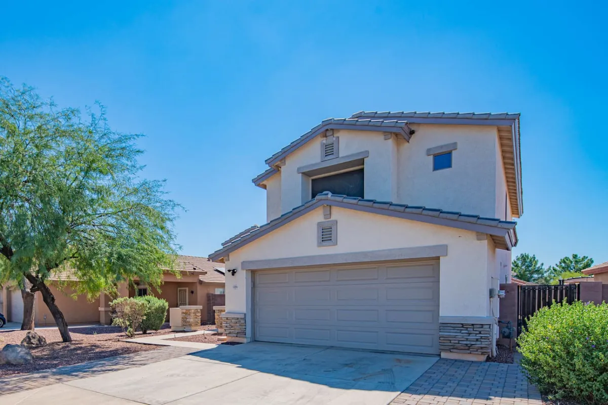 This exterior shot captures the front of the home with a welcoming garage door, stone accents, unique roofline, and surrounding greenery. It evokes a sense of arrival and hints at the social opportunities in the driveway or front yard, such as barbecues or morning coffee under the trees.