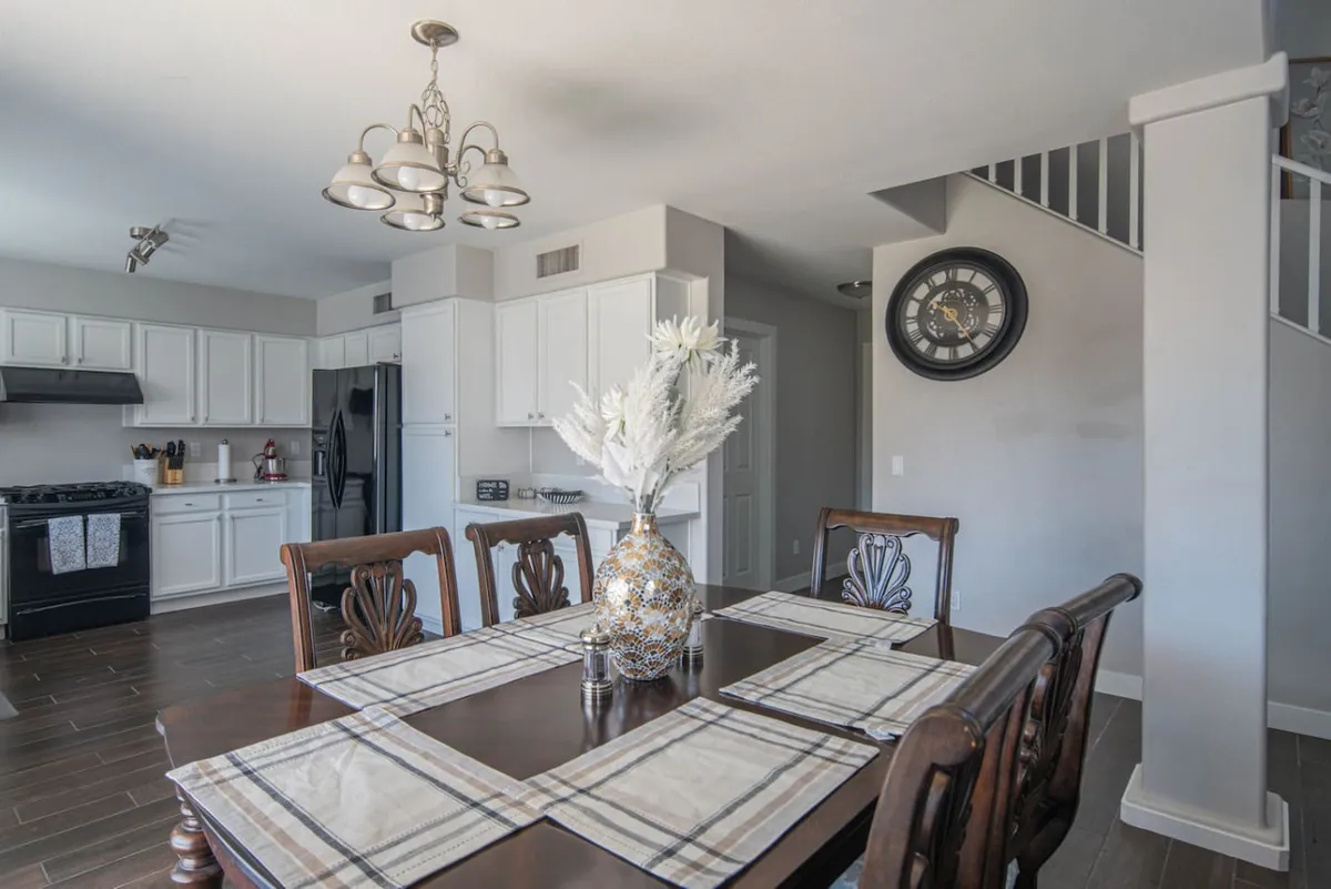 A close-up of the dining area, featuring a table for six set with a floral centerpiece and a wall clock. The space feels cozy and is designed for family meals, celebrations, or casual coffee catch-ups. It's positioned for easy access and social interaction.
