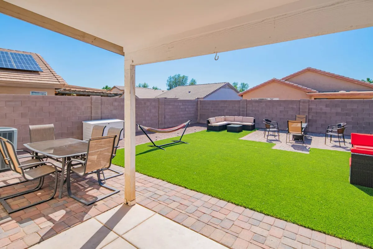 An exterior view of a spacious outdoor space with a hammock, lounge seating, dining table, and artificial grass. The inviting area is perfect for relaxing, entertaining, and socializing, with a mood that transitions easily from daytime lounging to nighttime stargazing.