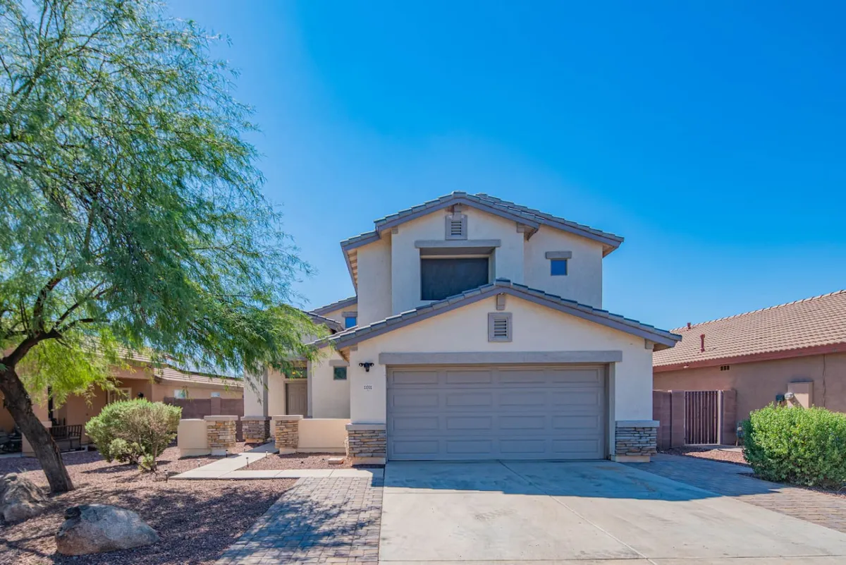 This image features the front façade of the home, including the garage door, landscaped yard, and surrounding trees. The view highlights the welcoming entrance and the overall curb appeal of the property, suggesting convenience and accessibility for new arrivals and departures.