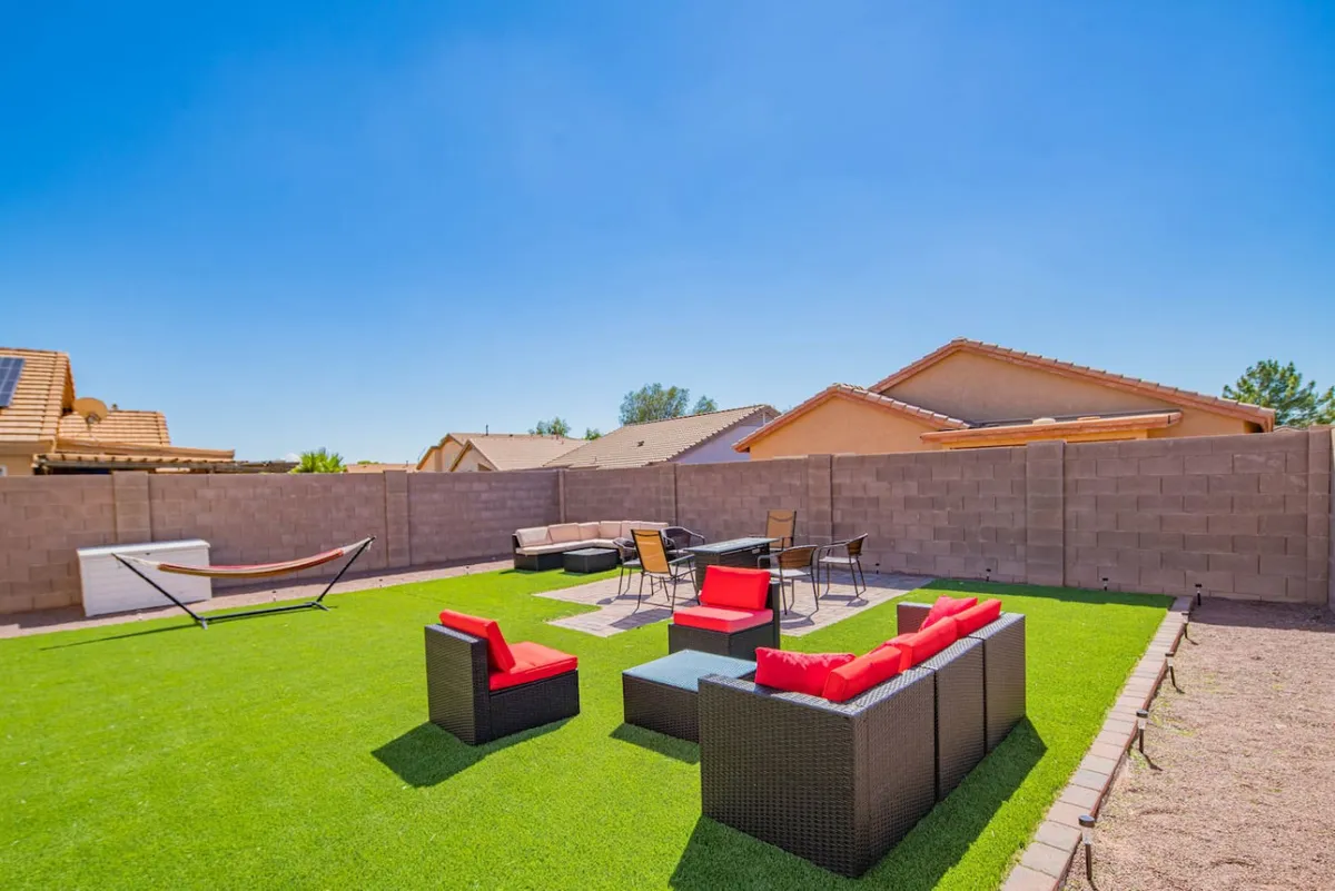 This exterior image showcases a backyard with red outdoor seating, a green lawn, a dining table, and a hammock. The area is clearly set up for outdoor relaxation, social gatherings, and enjoying time outside, with warm lighting hinting at both daytime and evening use.