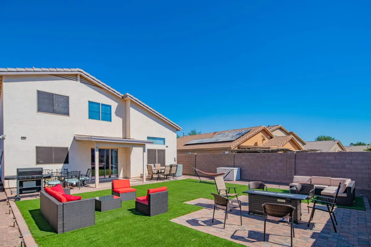 An inviting view of the backyard featuring patio furniture on a green lawn and the back of the house, designed for outdoor dining and relaxing. The setup hints at flexibility for both morning coffee in the sun and hosted parties during pleasant weather.