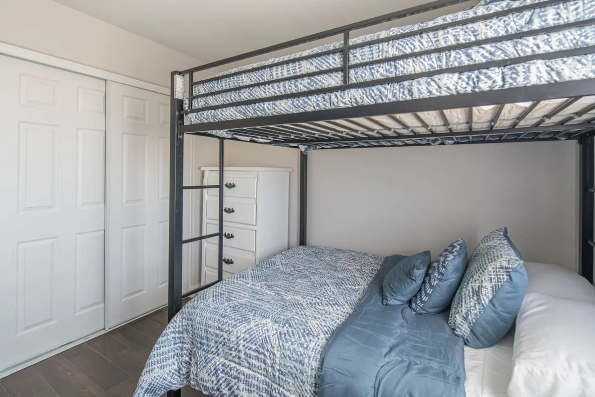 A playful and inviting bedroom with a bunk bed adorned with decorative pillows and a dresser nearby. The design is welcoming, ideal for children’s sleepovers or creating a fun retreat for younger guests.