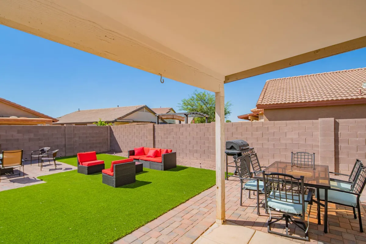 This exterior image showcases a vibrant red seating area, an outdoor dining table, and a grill on a backyard patio. The setup is ideal for outdoor dining, barbecuing, and relaxed social gatherings, with an inviting atmosphere for post-work relaxation or team-building events.